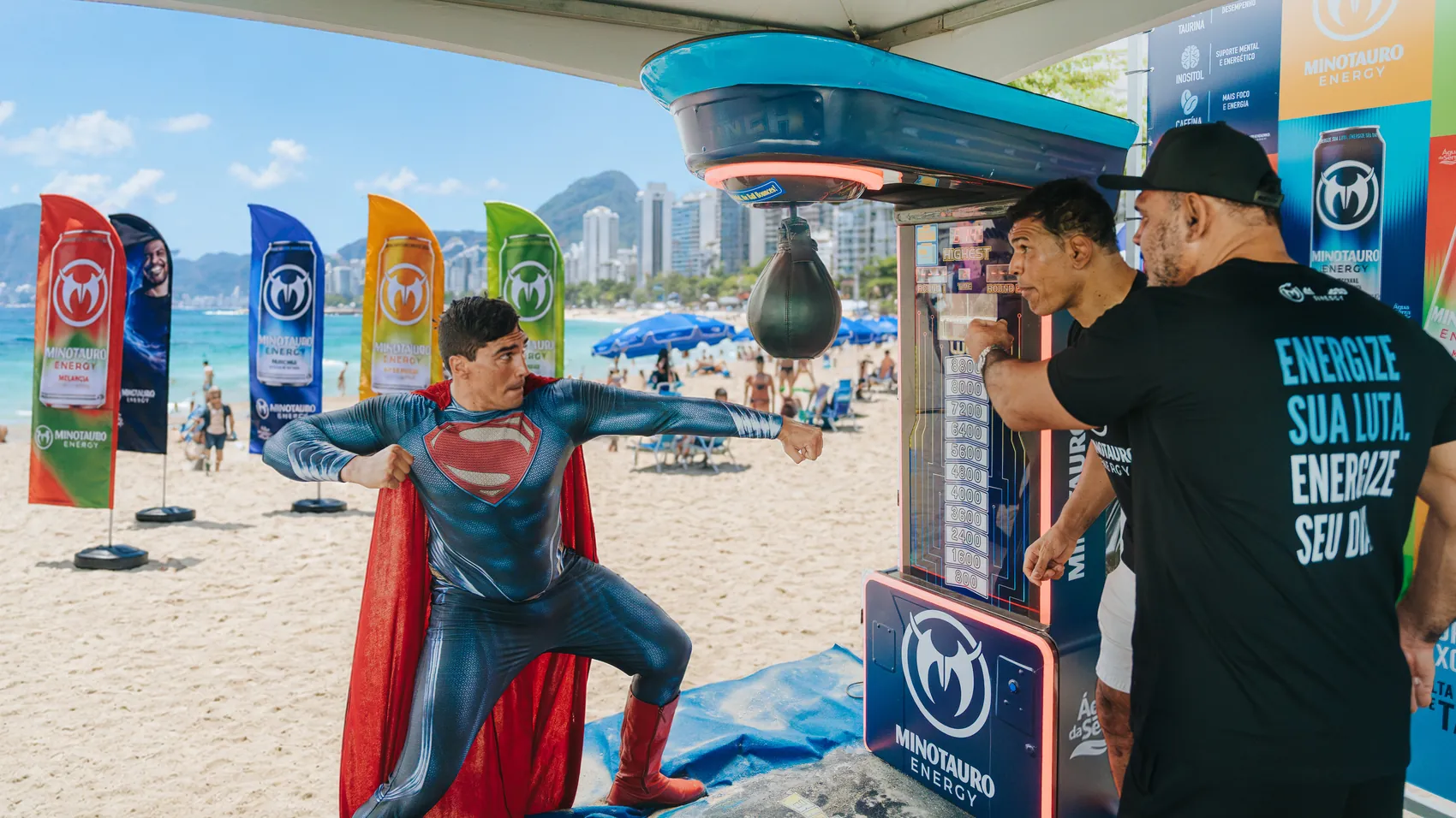 Ativação de marca Minotauro Energy em praia, com bandeiras dos cinco sabores e equipamento de treino de boxe